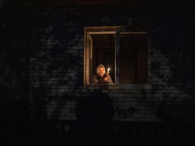 70-летняя Екатерина смотрит в окно, держа свечу в своем доме во время отключения электроэнергии, Бородянка, Киевская область, Украина, четверг, 20 октября 2022 года. Фото: Francisco Seco / AP
